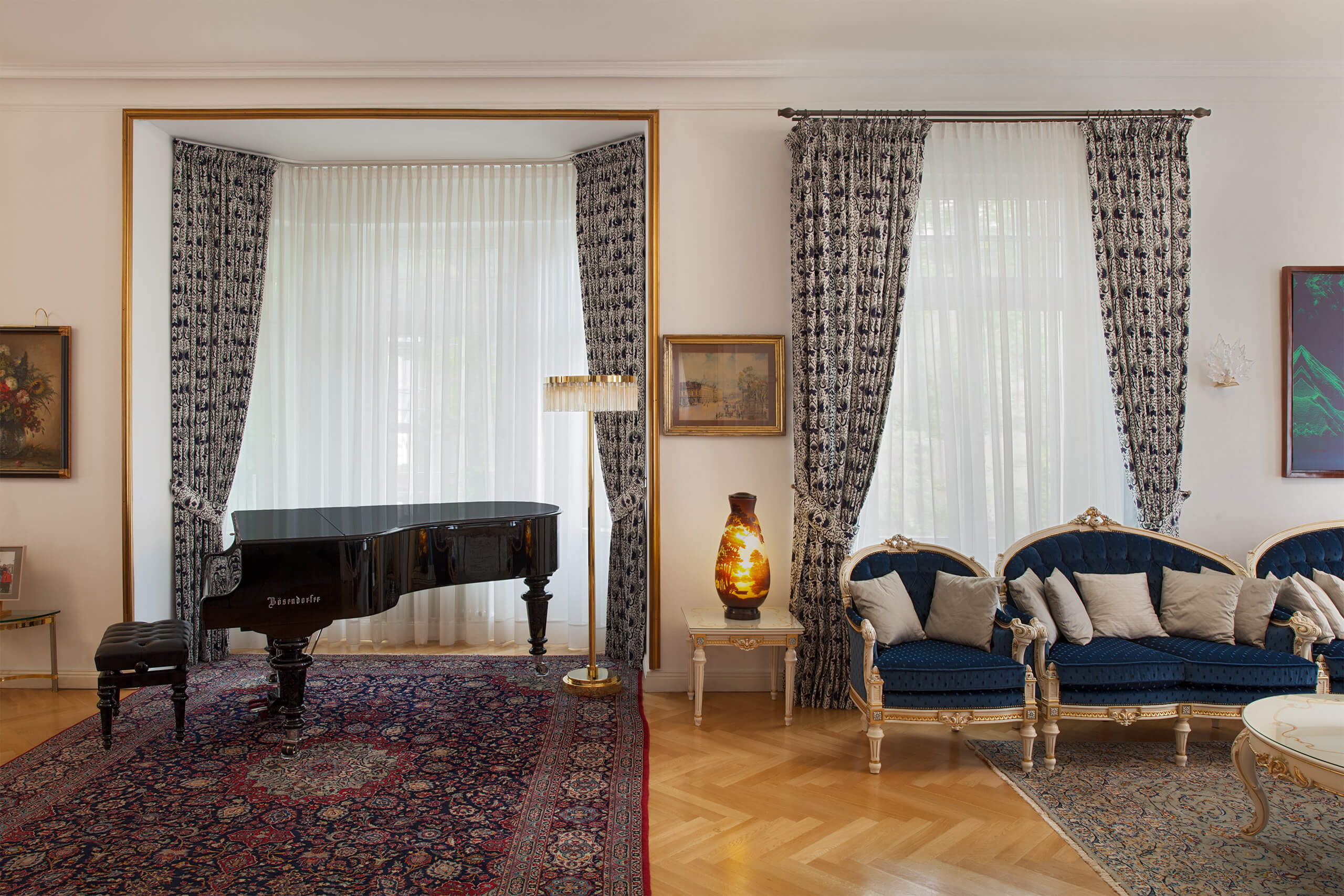 zwei Fenster mit Gardinen und gefütterten Vorhängen, davor steht ein Flügel auf einem klassischen Teppich